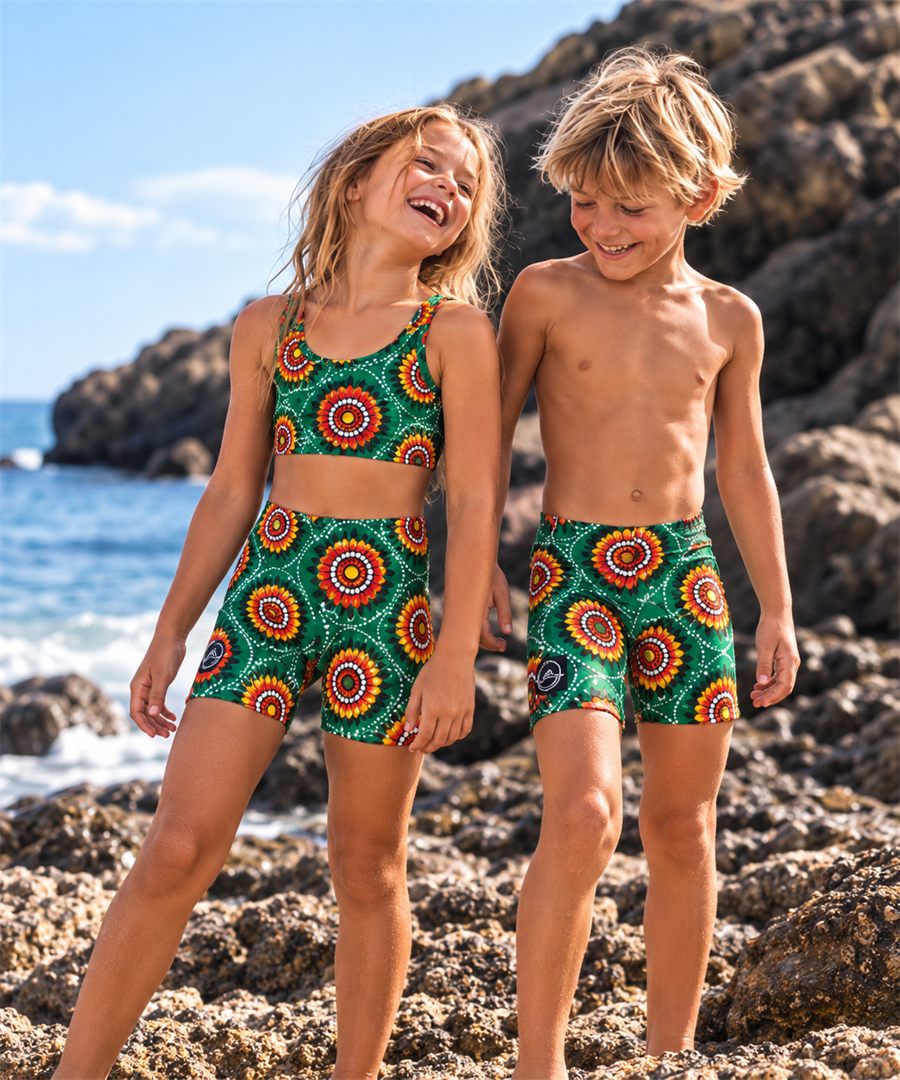 AI-generated visualisation: two children on rocks by the sea wearing a green medallion print, shorts and a matching crop top.